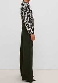 Haut à manches longues avec un motif abstrait noir et crème, assorti à un pantalon noir taille haute à jambes larges et des talons noirs pointus.