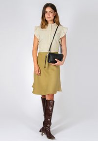 Blusa a righe con maniche a volant, gonna verde oliva e stivali marroni fino al ginocchio. Borsa a tracolla nera con cinturino. Tessuto morbido e design elegante.