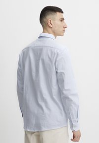 Camisa de manga larga a rayas en azul claro con cuello clásico. Presenta puños con botón y corte recto. Tejido de algodón suave. Vista trasera.