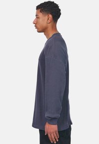 Camisa de manga larga de canalé en gris oscuro con cuello redondo, que presenta un corte holgado y costuras visibles.