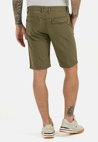 Olivgrüne Shorts mit gerader Passform und zwei Gesäßtaschen, getragen mit hellgrauen Schuhen, die eine schwarz-weiße Akzentlinie haben.