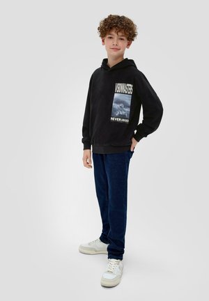 Un sweat à capuche noir avec un design graphique comprenant du texte et une image, associé à un pantalon bleu foncé et des baskets blanches. Tissu doux, coupe décontractée.