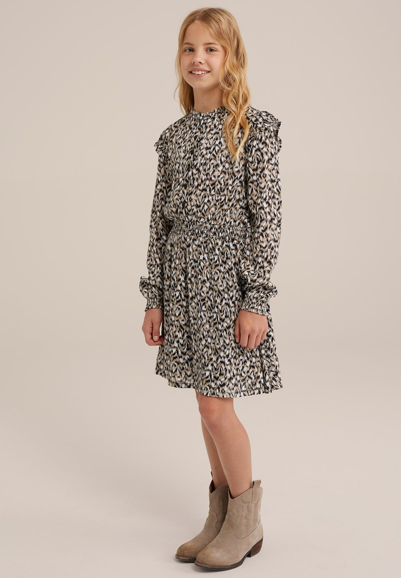 Langärmliges schwarzes Kleid mit beigen und blauen abstrakten Mustern, mit Rüschenschultern und gerafftem Taillenbund, kombiniert mit hellbraunen Knöchelschuhen.