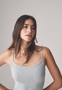 Šedé rebrované tielko s tenkými ramienkami, priliehavý strih a hladká textúra. Jednoduchý, univerzálny kúsok na jednofarebnom pozadí.