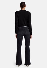 Jeans neri a vita alta svasati con una texture liscia, cinque tasche e una cintura nera elegante, abbinati a un top fitted a maniche lunghe nero.