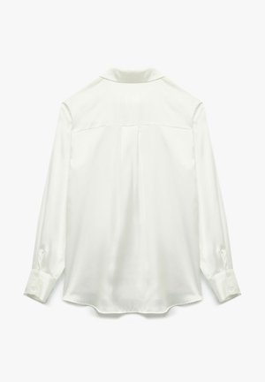 Camisa blanca de satén de manga larga con cuello, que presenta un yugo trasero, un discreto detalle de pliegue y puños abotonados para el cierre.
