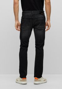 Jeans slim-fit scuri con una trama liscia e un leggero scolorimento, dotati di due tasche posteriori e una vita con logo. Indossati con sneakers chiare.