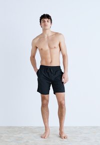 Shorts de bain noirs en tissu léger, dotés d'une taille élastique avec un cordon de serrage et de poches latérales pour plus de commodité.
