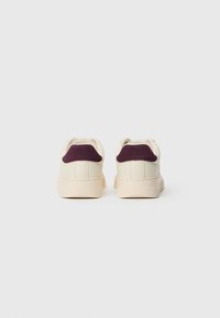 Μπεζ αθλητικά παπούτσια με υφή σε λευκό τόνο και σκούρες μωβ σουέτ λεπτομέρειες στη φτέρνα. Ελαφρύς πάτος με ραβδωτές υφές.