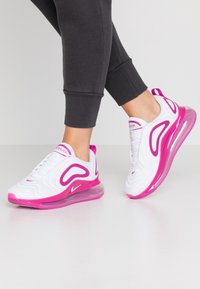 Baskets blanches avec des accents roses, dotées d'une tige texturée, d'une semelle rembourrée et d'une unité d'air visible dans le talon.