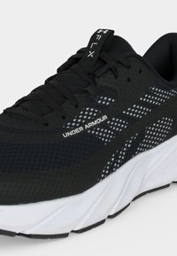 Μαύρο παπούτσι για τρέξιμο Under Armour με λευκή σόλα, αναπνεύσιμο επάνω μέρος από δίχτυ και μαύρα κορδόνια, με το όνομα της μάρκας στο πλάι.