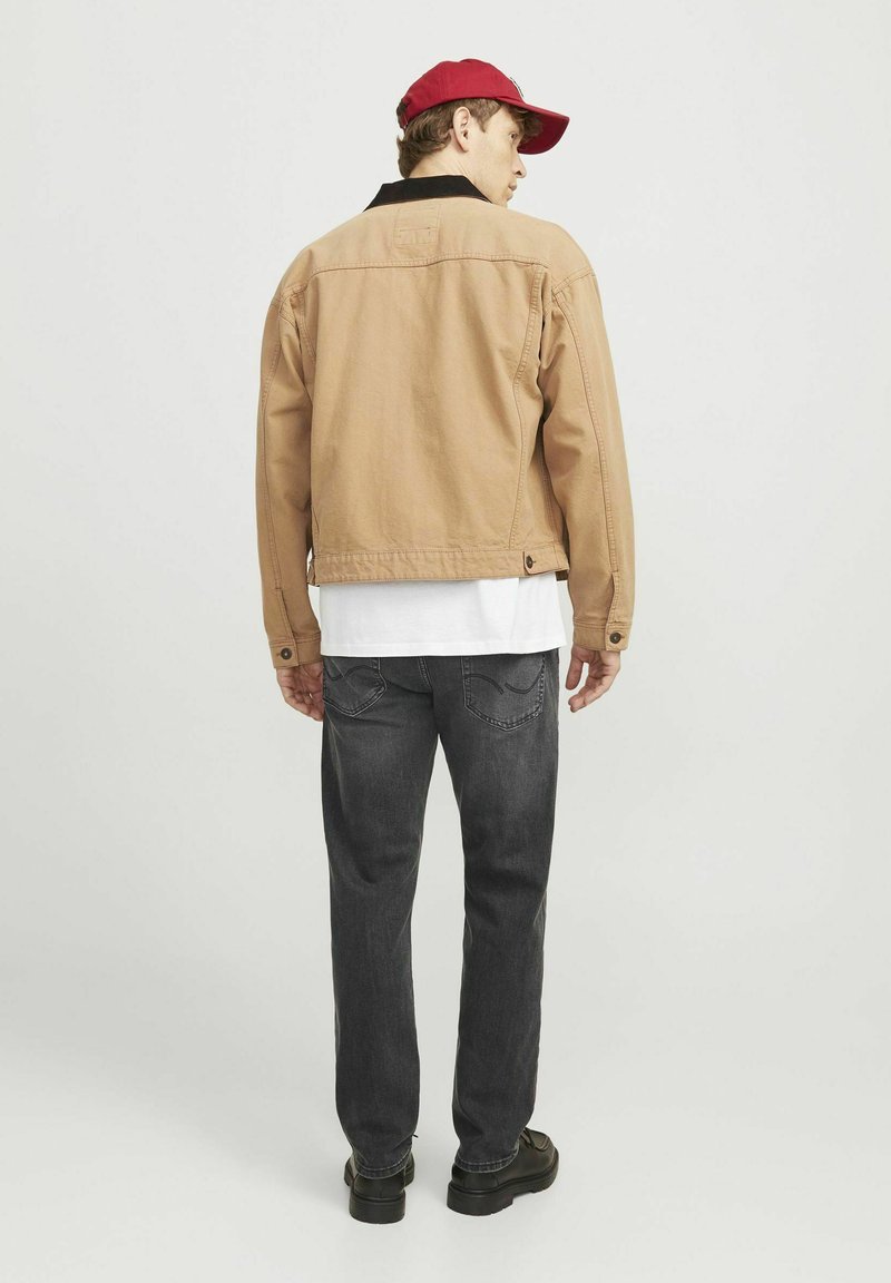 Beige Jacke mit schwarzem Kragen, taillierte Form und Knopfdetails, kombiniert mit dunkelgrauen Jeans und schwarzen Schuhen, von hinten betrachtet.