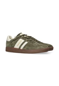 Groene suède sneakers met crème accenten, voorzien van twee witte strepen en een gestructureerde bruine rubberen zool. Merken worden weergegeven op de zijkant.