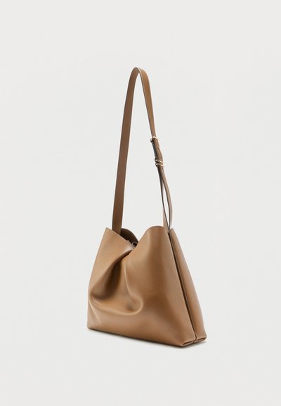 Μαλακή τσάντα ώμου από ταμπά δέρμα με έναν ρυθμιζόμενο ιμάντα και χαλαρή, διπλωμένη σχεδίαση σε απλό φωτεινό φόντο.