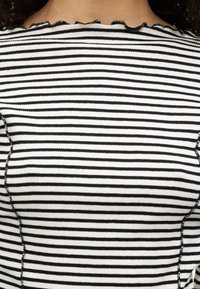 Čierno-biele pruhované tričko s rebrovanou textúrou, so zvlneným výstrihom a viditeľným prešitím pozdĺž bokov.