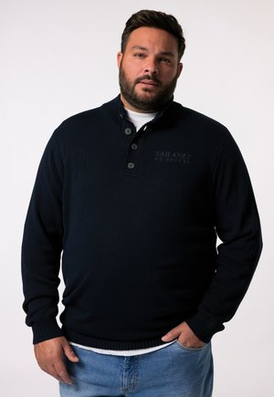 Marineblauwe gebreide pullover trui met een hoge kraag, drie-knops sluiting en geribbelde boorden. Voorzien van een reliëf logo detail op de borst.