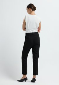 Zwarte getailleerde broek en een witte mouwloze top met een gestructureerd ontwerp. De outfit heeft een soepele textuur en een aansluitende silhouet.
