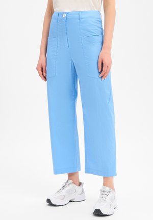Pantalon bleu clair à jambes droites avec poches plaquées, porté avec des baskets blanches de sport et un haut blanc.