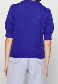 Kungsblå stickad tröja med korta puffärmar och en ribbad krage. Tillsammans med ljusblå jeans som visar en avslappnad passform.