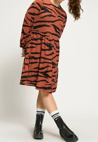 Sukienka typu T-shirt w kolorze rdzawym z czarnymi paskami w zebrę. Posiada długie rękawy, luźny krój oraz dwie boczne kieszenie. Do tego czarne botki za kostkę.