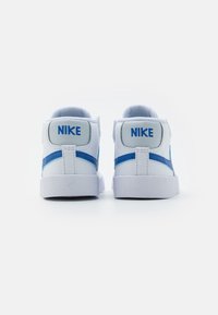 Vita sneakers med blå accenter, med en texturerad sula, vadderad krage och en framträdande logotyp på hälen och sidan.