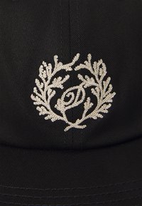 Casquette noire ornée d'un logo brodé argenté avec un design circulaire composé de branches et de brindilles, agrémenté de petits points et d'accents tourbillonnants.