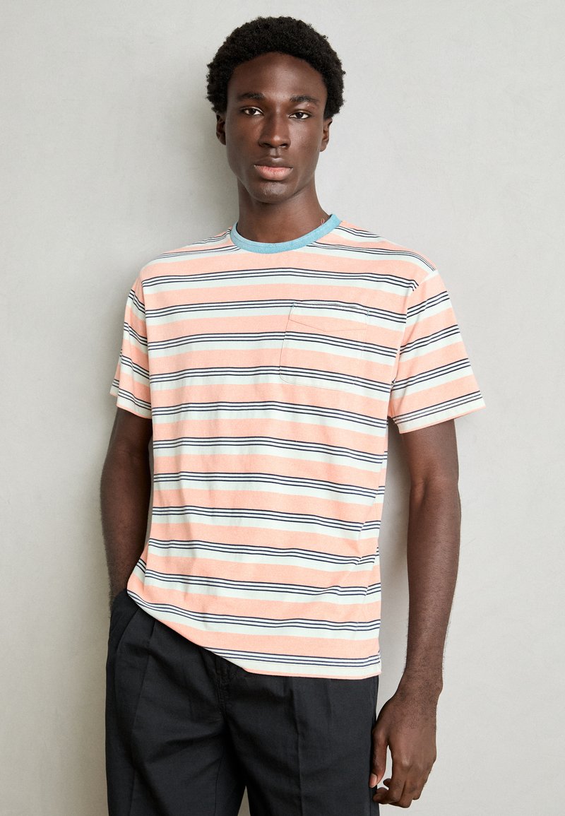 Stribet t-shirt i pastel orange, blå og hvid. Rund halsudskæring, korte ærmer og lille brystlomme detalje.