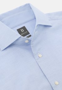 Gai zila teksturēta krekla ar izklātu apkakli, kas rotāta ar baltām pogām un birku ar uzrakstu "BOGGI MILANO."