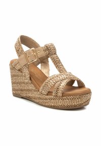 Sandalia cuña con parte superior de paja trenzada en beige claro, con tiras entrelazadas y un toque de hebilla dorada sobre una suela de plataforma lisa.