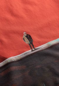 T-shirt en tissu rouge-orangé avec une illustration imprimée d'une personne portant une veste, se tenant sur un paysage stylisé.