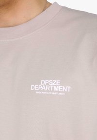 Világos bézs pulóver, bordázott kerek nyakkal, a mellrészen fehér hímzéssel "DPSZE DEPARTMENT" és "MADE FOR ELITE HUSTLERS" felirattal.