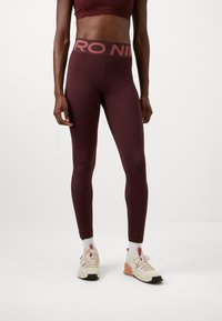 Leggings bordeaux taille haute avec une texture lisse et des coutures plates, présentant un logo "NIKE" rose clair sur la ceinture.