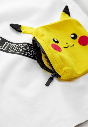 T-shirt bianca con una tasca di Pikachu gialla con accenti neri, dettagli facciali ricamati e chiusura con zip. Etichetta nera stampata visibile.