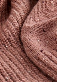 Gestrickter Stoff in einem sanften rosa-braun mit einem strukturierten, gerippten Muster und verstreuten weißen und dunklen Einsprengseln. Weiche, fuzzige Textur.