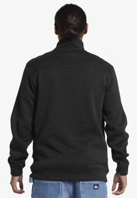 Čierna fleecová mikina s vysokým golierom, rebrovanými manžetami a jemnou textúrou. Má logo nášivku blízko lemu.