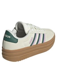 White suede sneaker with green and pink stripes, featuring a thick gum rubber sole and padded collar. Branding on the heel and tongue.
