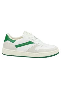 Basket blanche basse avec des accents verts, lacets à l’avant et semelle texturée, vue de côté sur fond blanc.