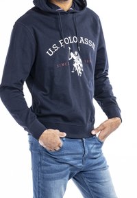 Marinblå hoodie med snörning, prydd med en vit polo-spelart grafisk design och texten "U.S. POLO ASSN. SINCE 1890" i kontrasterande färger.