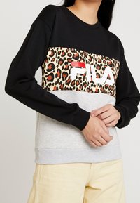 Czarna i szara bluza z panelem w panterkę, na którym znajduje się czerwono-białe logo "Fila". Ściągacze na mankietach i dole, miękki bawełniany materiał.