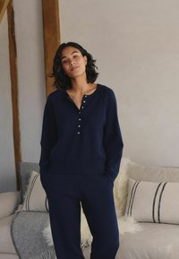 Navy blue, long-sleeve sweater with a rounded neckline and button front. Soft fabric and relaxed fit, paired with matching pants.