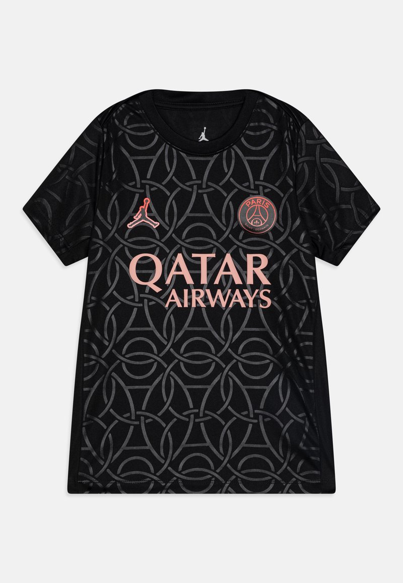 Melnā jakā, kurai ir spilgts savienotu loku raksts. Tajā ir rozā logotips Qatar Airways un Jordānijas emblēma.