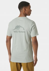 Camiseta de color gris claro con mangas cortas, que presenta un diseño gráfico de montañas y un sol en la parte posterior, hecha de una suave mezcla de algodón.