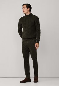 Pull à col montant en maille torsadée vert foncé, associé à un pantalon slim vert foncé et des bottines en daim marron. Design simple et matériau texturé.