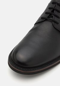 Schwarzer Lederschuh mit runder Spitze, glatter Textur, kontrastierenden braunen Nähten entlang der Sohle und traditionellem Schnürdesign.