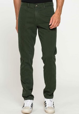 Pantaloni di cotone verde scuro a vestibilità slim, con chiusura a bottone, passanti per cintura e tasche laterali. Abbinati a sneaker bianche.