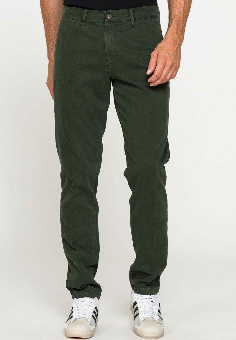 Pantaloni di cotone verde scuro a vestibilità slim, con chiusura a bottone, passanti per cintura e tasche laterali. Abbinati a sneaker bianche.