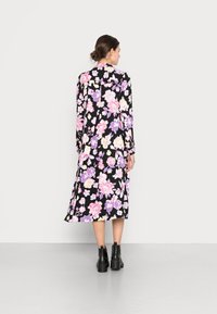 Vestido midi floral com fundo preto e flores rosas e roxas, mangas longas e gola alta, combinado com botas ankle pretas.