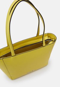 Gul læder tote taske med to sorte side accenter, lynlåslukning og Calvin Klein logo på fronten. Glat tekstur og struktureret form.