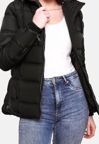 Svart puffjacka med huva, med quiltade paneler, dragkedja fram och elastiska ärmslut. Kombineras med högmidjade blå jeans.