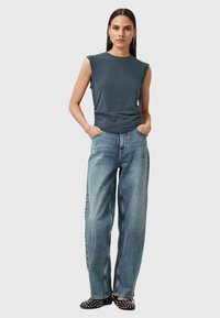 Grå ærmeløs top med rund halsudskæring, parret med løse lyseblå jeans og sorte flade sko dekoreret med sølvnægle.